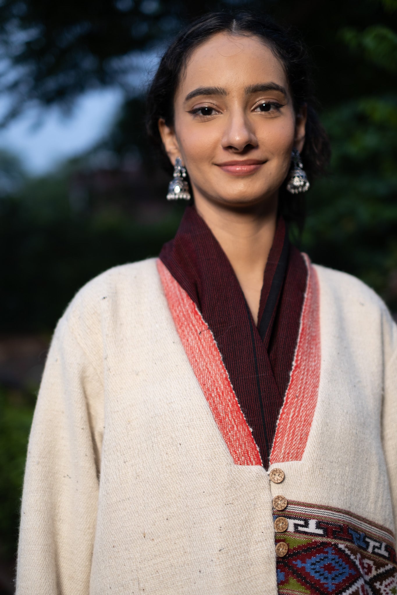 Woman wearing a cream-colored  Coat with a patterned trim, standing outdoors.